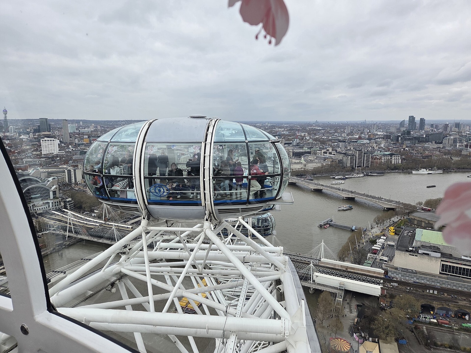 A glass capsule of the London Eye high above the Thames, with the city spread out behind it.