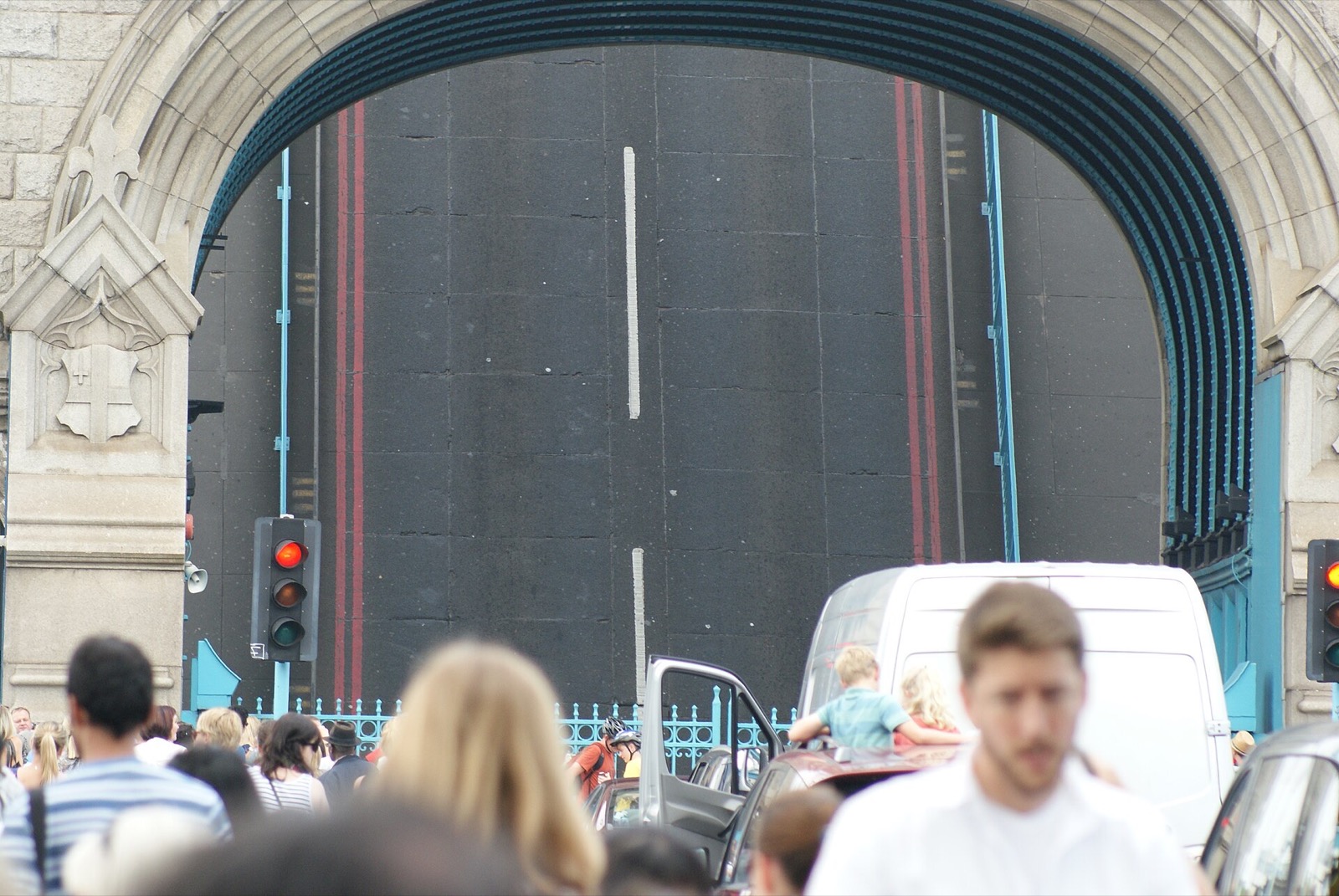 One half of the roadway of Tower Bridge raised to let a ship through, with people waiting at the barrier.