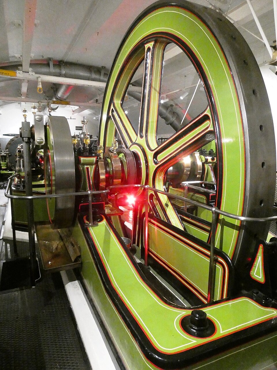 A green and red steam engine with a great flywheel in the engine rooms of Tower Bridge.