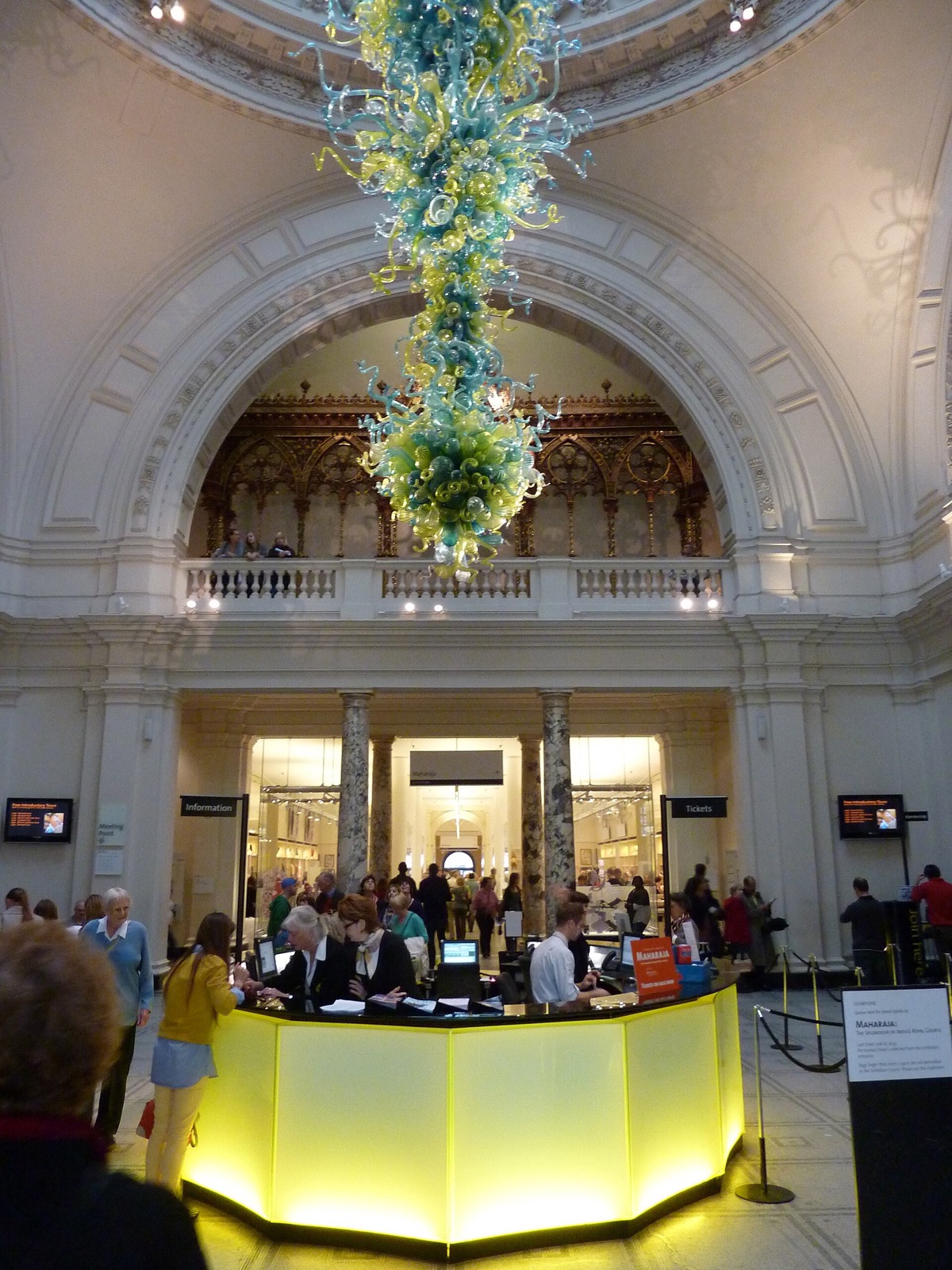 The entrance hall of the Victoria and Albert Museum, with a blue and green glass chandelier hanging under the dome.
