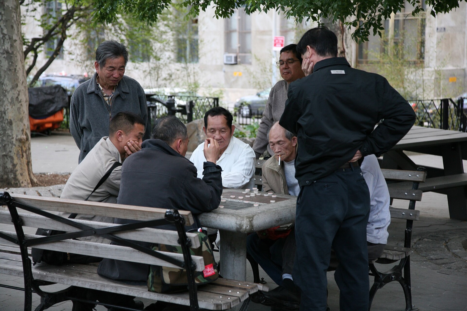 Men gathered round a game of Chinese chess at a table in Columbus Park.