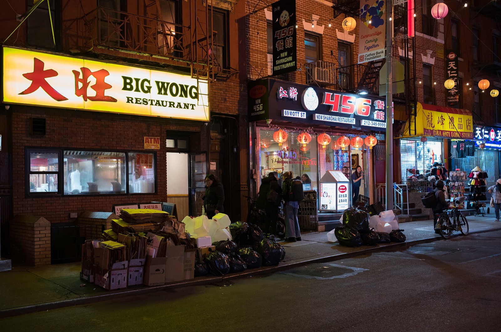 Mott Street in Chinatown after dark, with lit shop signs and strings of lights across the street.