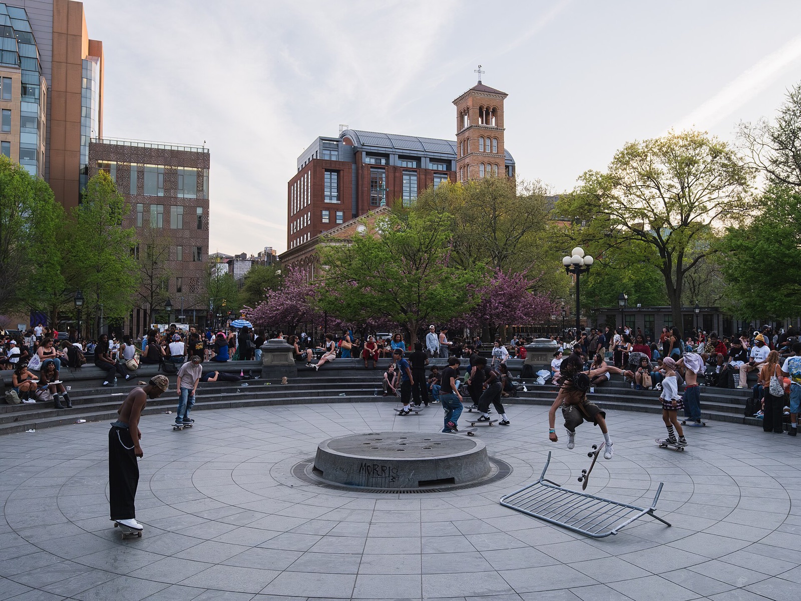 Skateboarders and people sitting round the dry basin of the fountain in Washington Square Park.