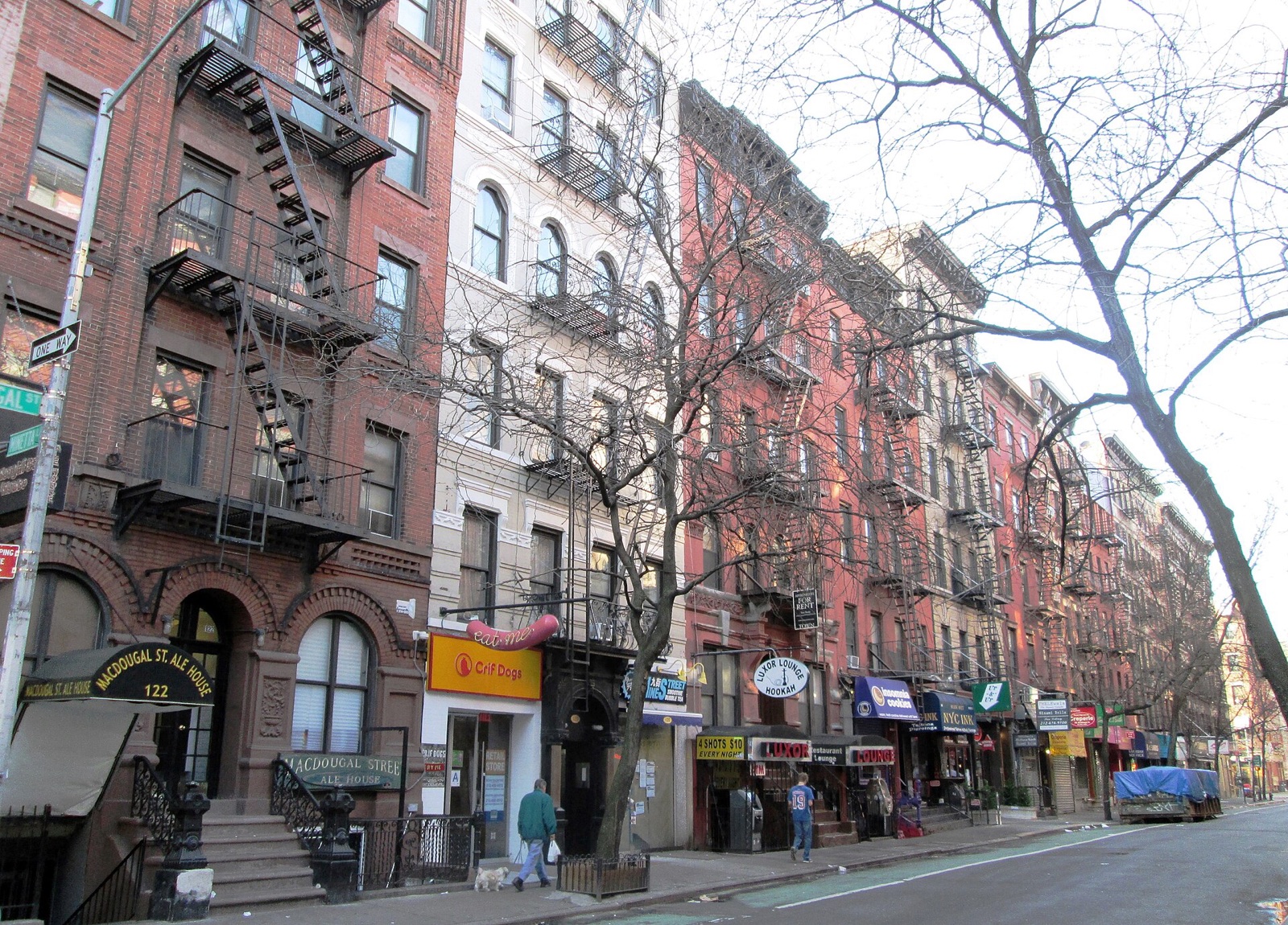 Old tenement buildings with fire escapes and shops along MacDougal Street.