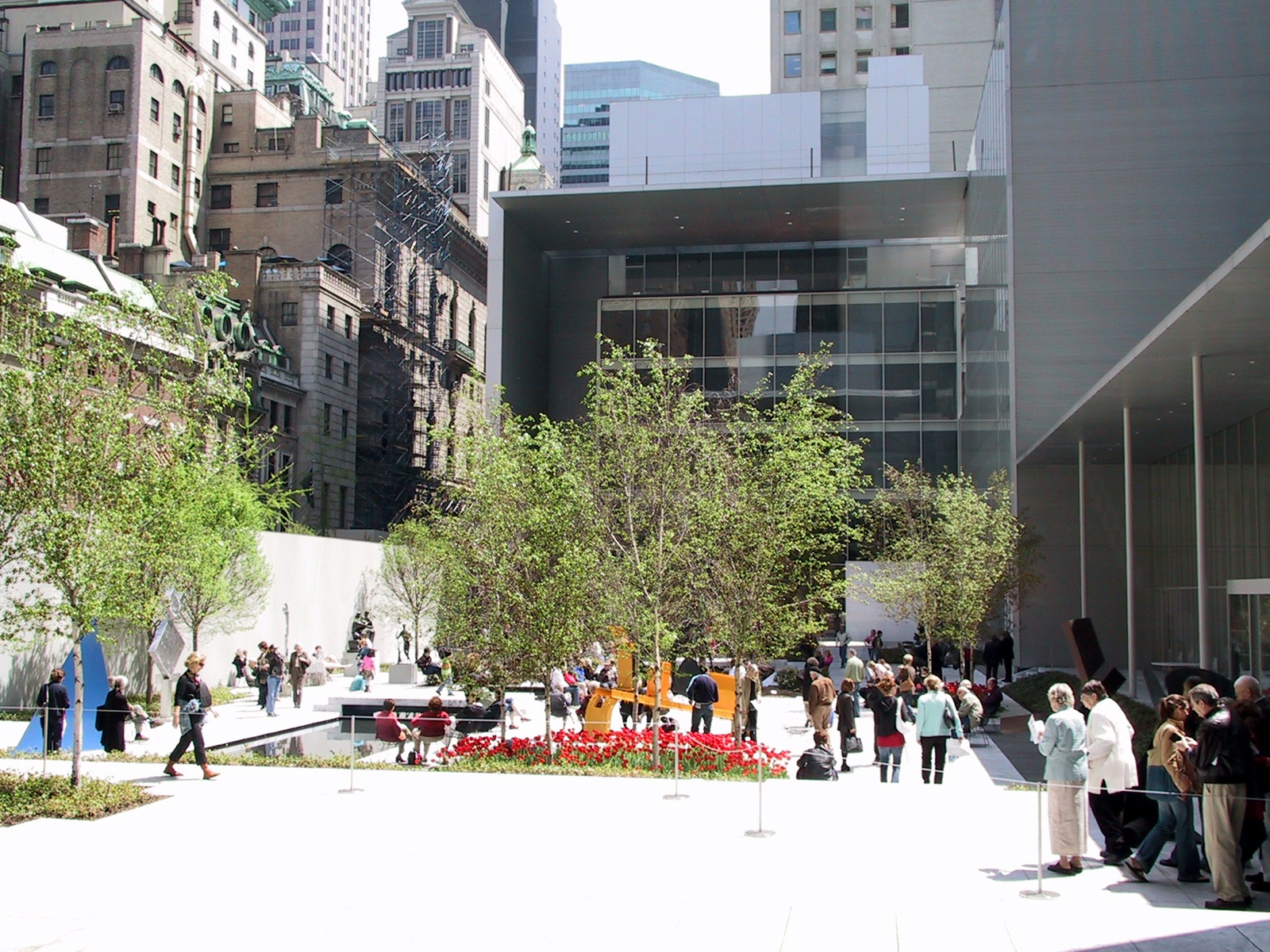 The sculpture garden of the Museum of Modern Art, with visitors among trees and pools and the museum's glass wall behind.