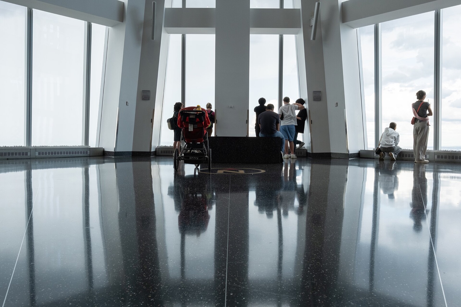 Visitors in One World Observatory, dark against the windows that run from floor to ceiling.