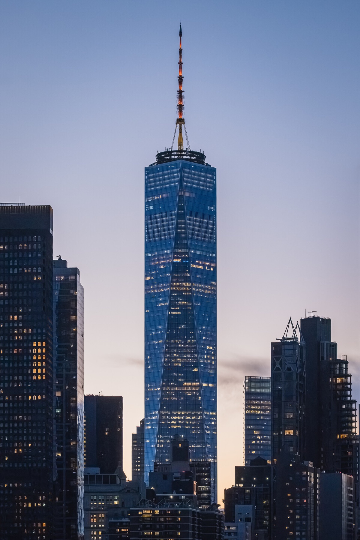 One World Trade Center at dusk, its glass lit from within, above the buildings of Lower Manhattan.