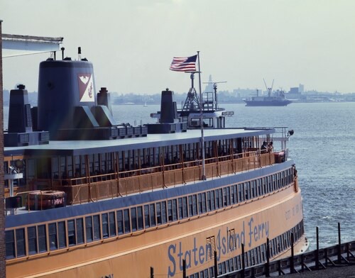 The side of a Staten Island Ferry seen from another boat, its name painted on the orange hull.