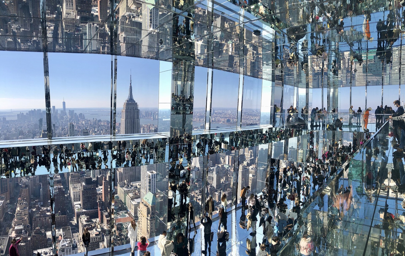 Visitors in the mirrored rooms of SUMMIT One Vanderbilt, with the skyline and the Empire State Building reflected above and below them.