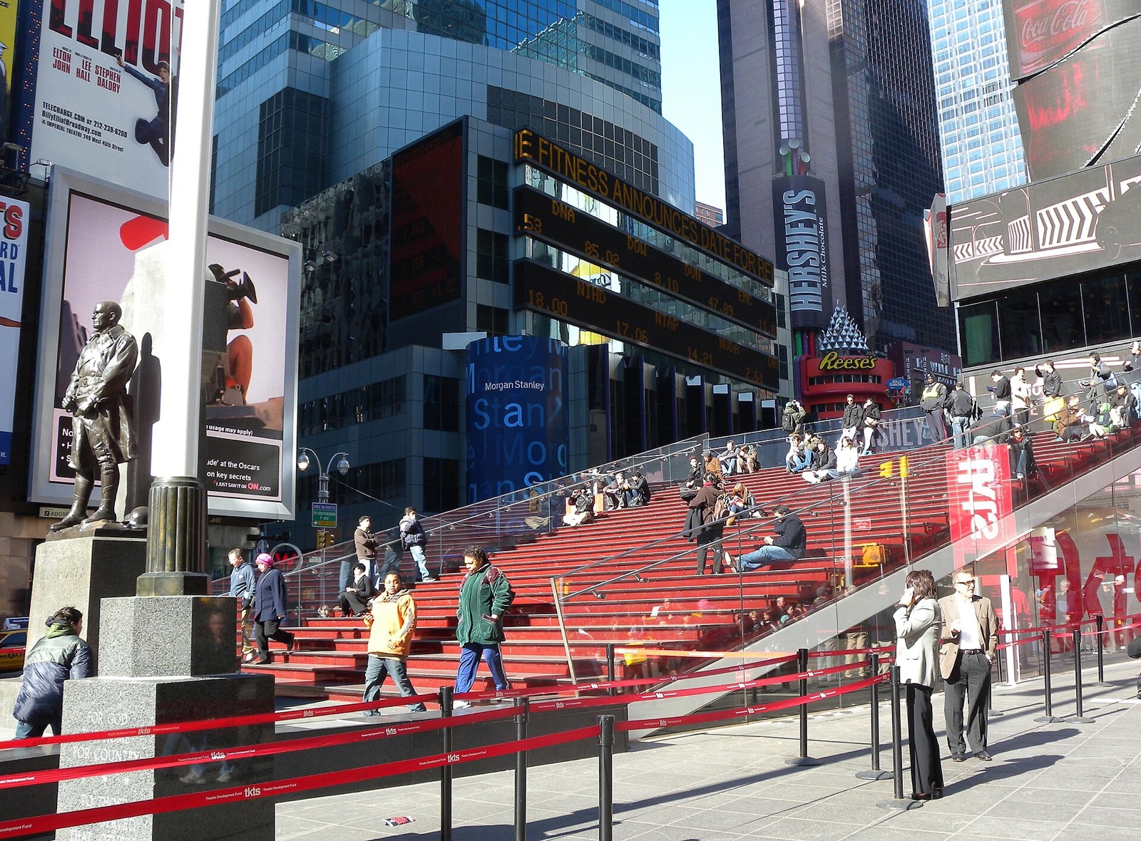 The red glass steps over the theatre ticket booth in Times Square, with people sitting on them.