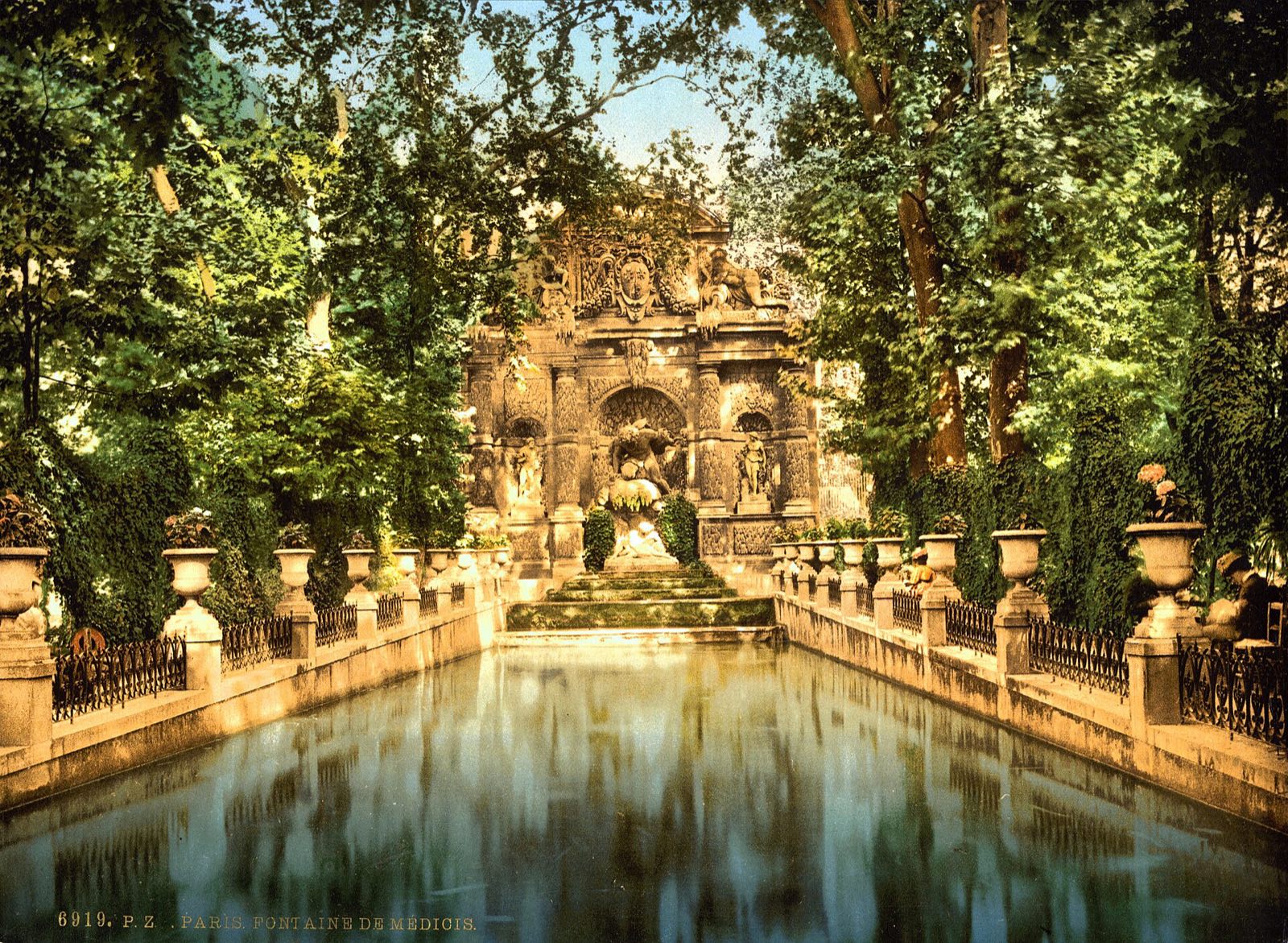 The Medici Fountain in the Luxembourg Gardens around 1900, a long basin under trees, in an early colour print.