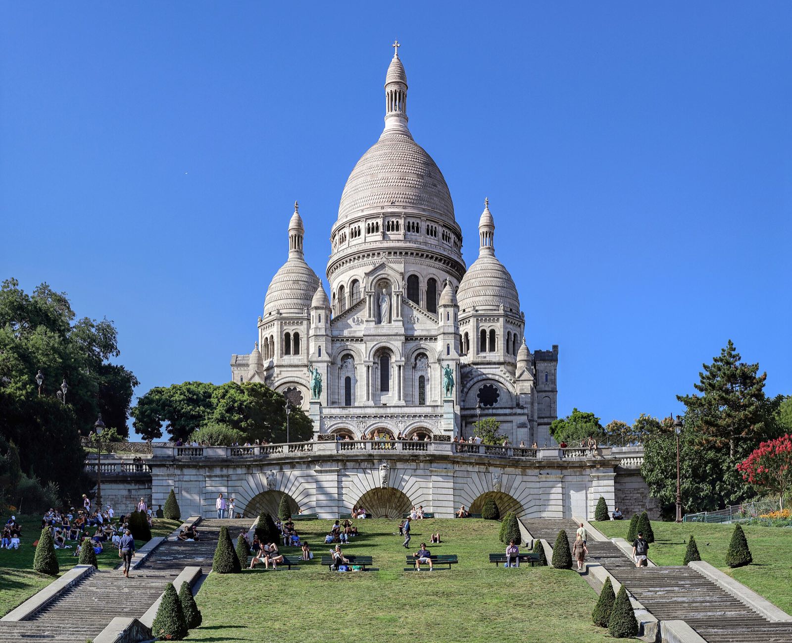 The white domes of the Sacré-Cœur basilica above the gardens on the hill of Montmartre, under a blue sky.