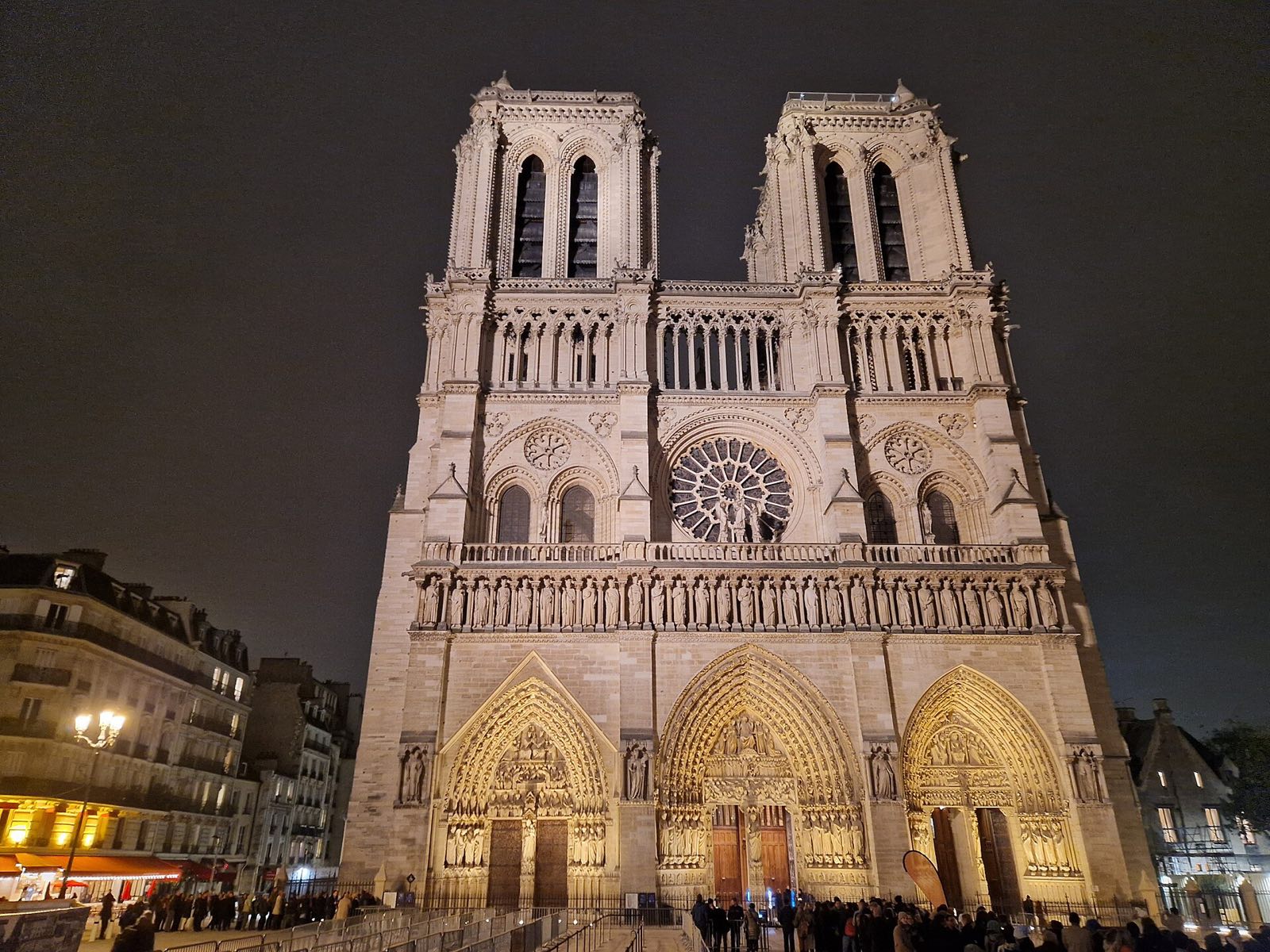 The west front of Notre-Dame de Paris lit at night, its two towers and rose window above the three portals.