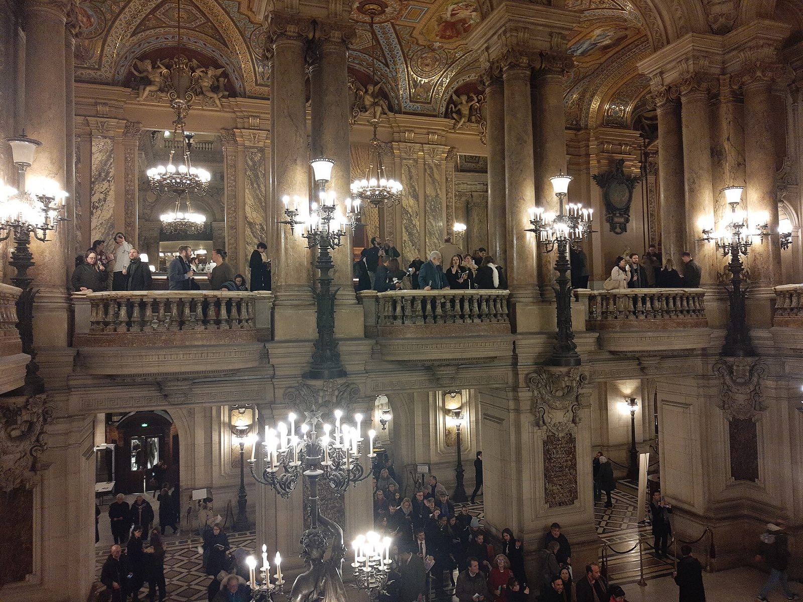 The grand staircase of the Palais Garnier seen from above, with visitors on the steps.