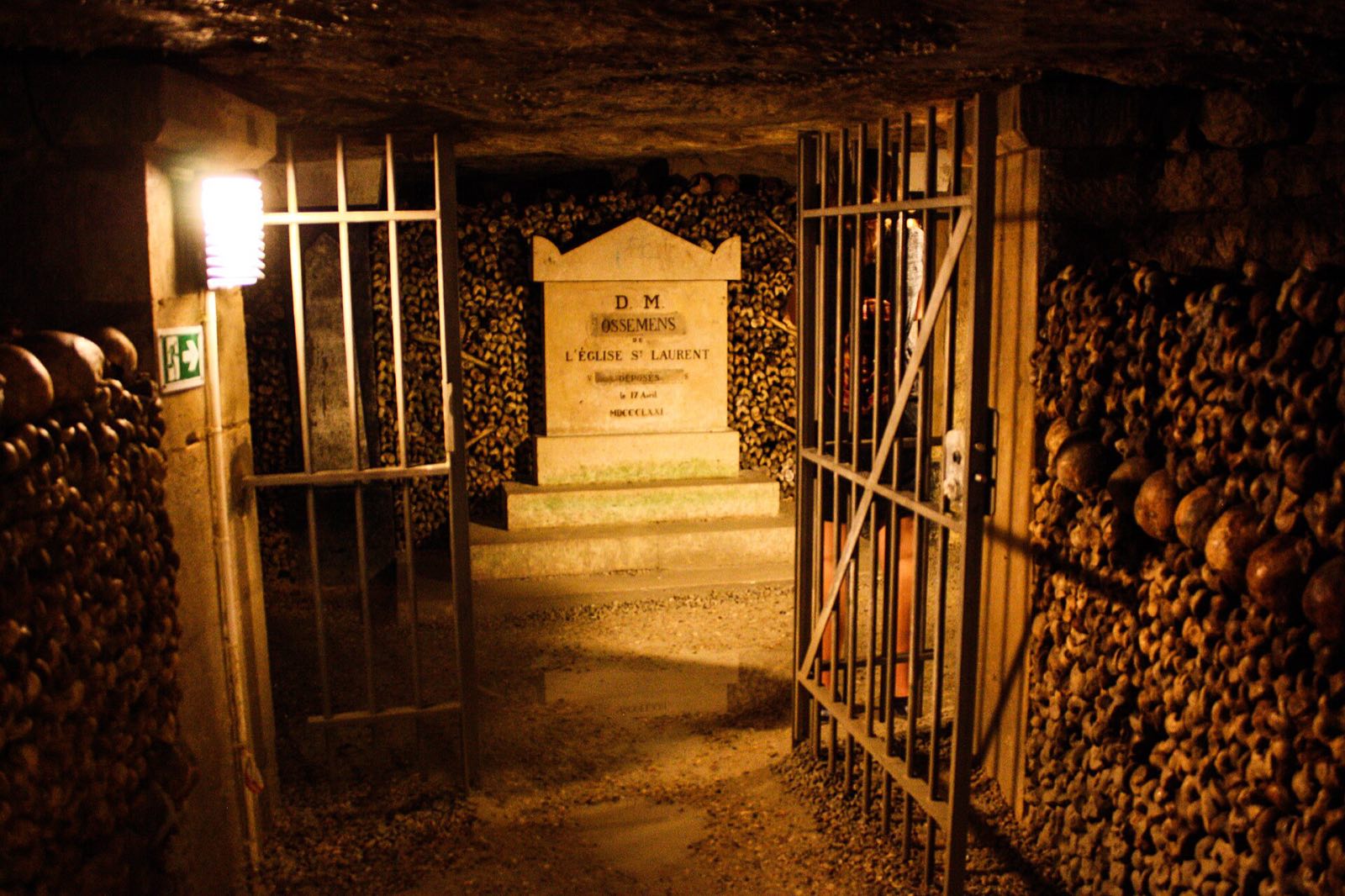 A gallery in the Catacombs of Paris, bones stacked to the ceiling on both sides of a gated tomb.
