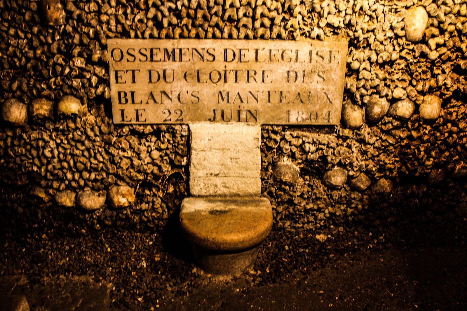 A wall of skulls and bones in the Catacombs of Paris, around a stone plaque naming the cemetery they came from.