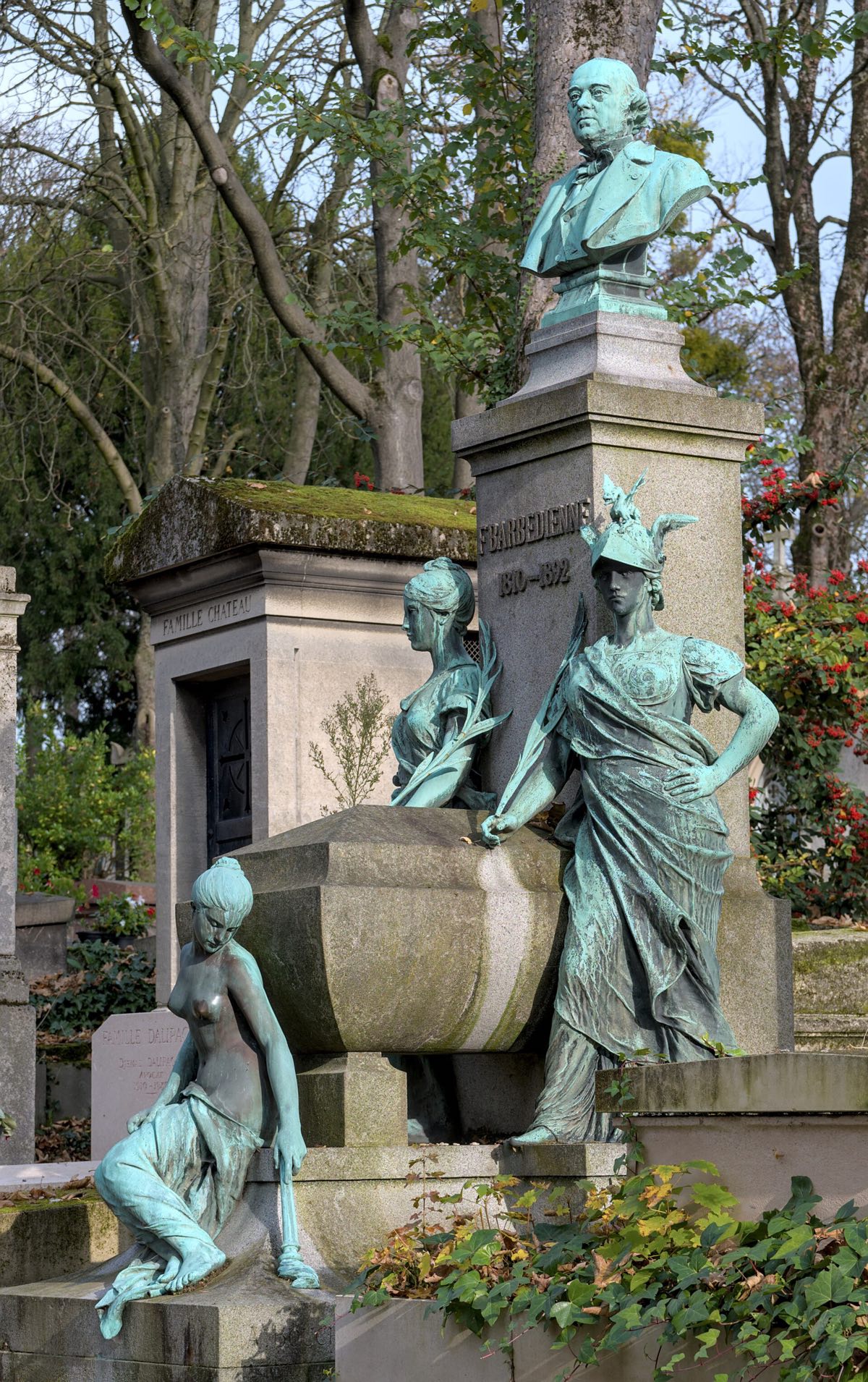 A tomb with bronze figures at Père Lachaise Cemetery, under trees.