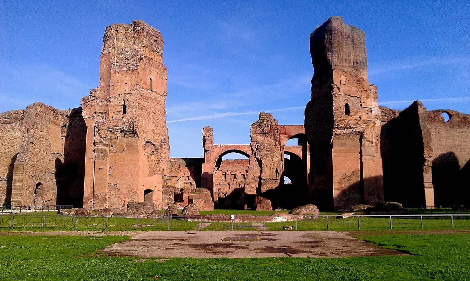 The ruined brick halls of the Baths of Caracalla seen across a lawn.