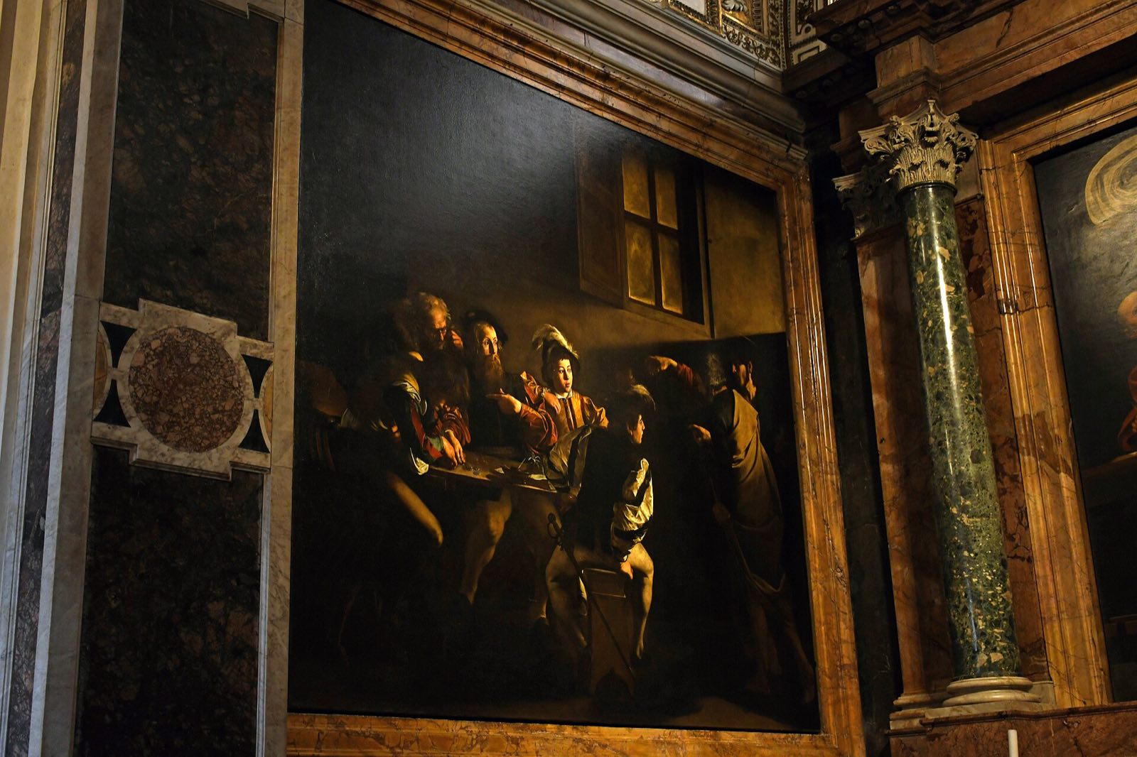 Caravaggio's paintings in the dark of the Contarelli Chapel, framed in coloured marble.