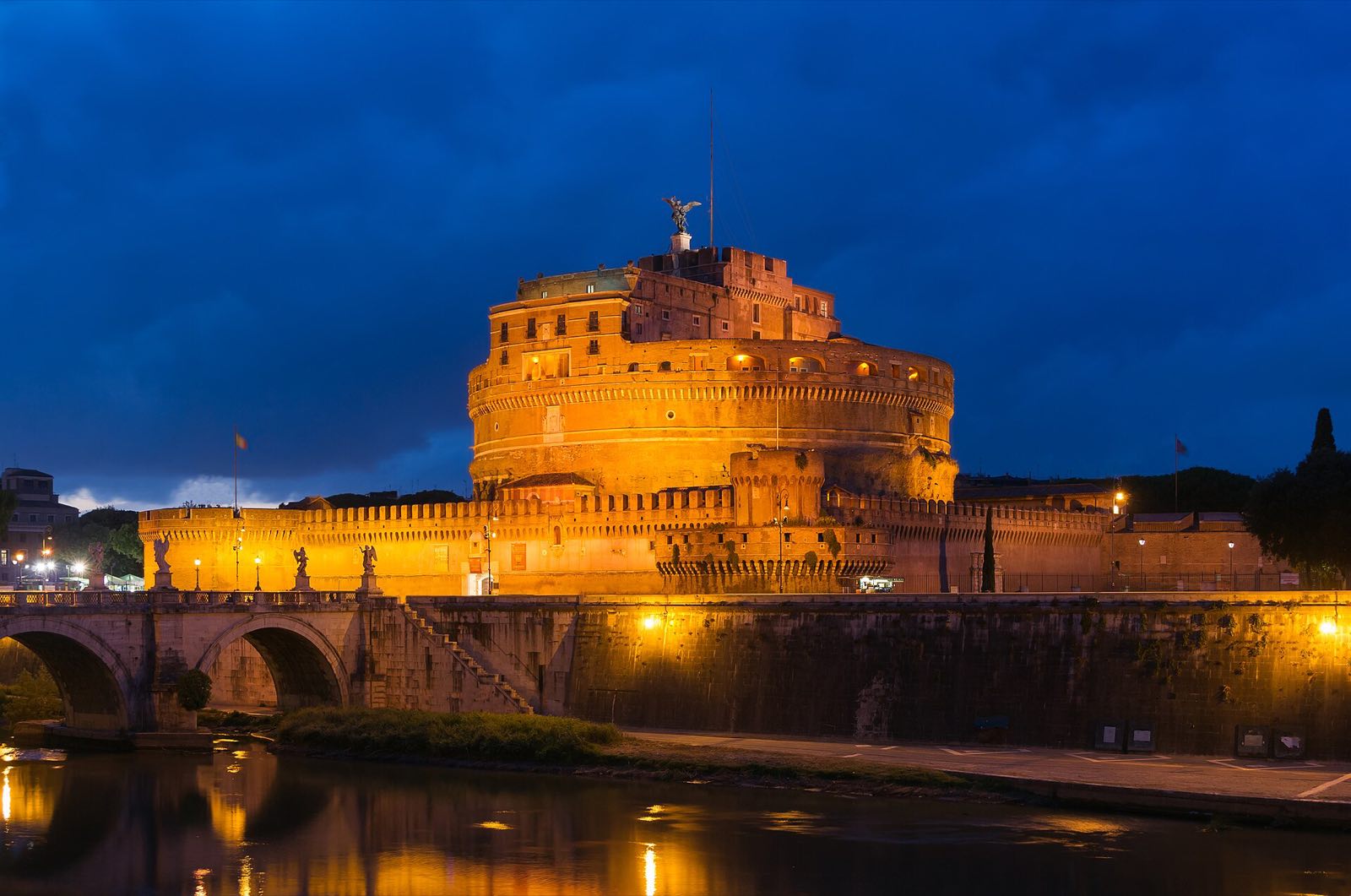 Castel Sant'Angelo lit at dusk, a round fortress under a deep blue sky.