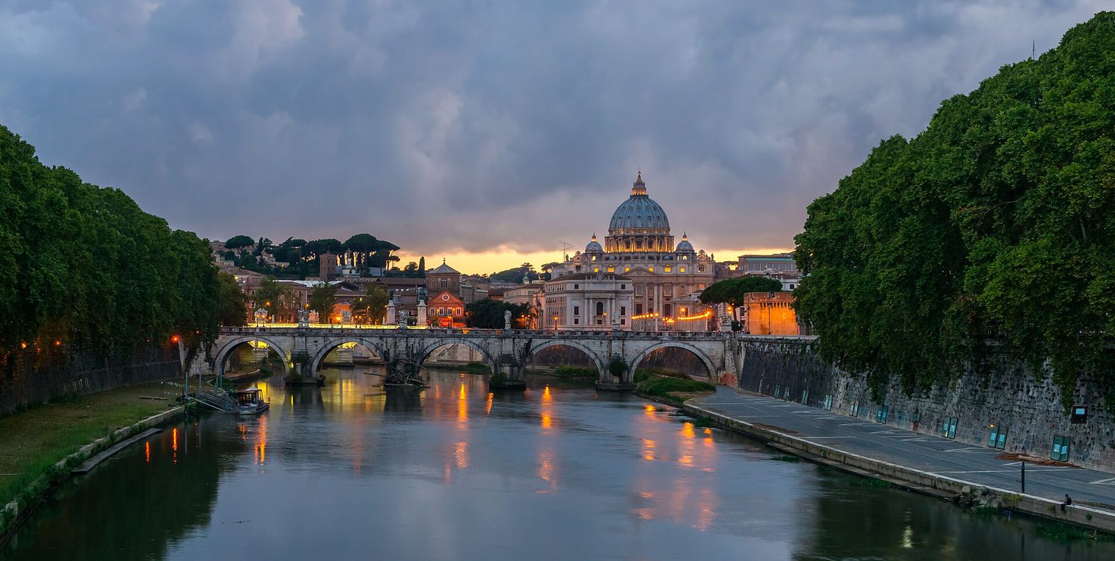 The Ponte Sant'Angelo over the Tiber at dusk, with the dome of St Peter's beyond it.