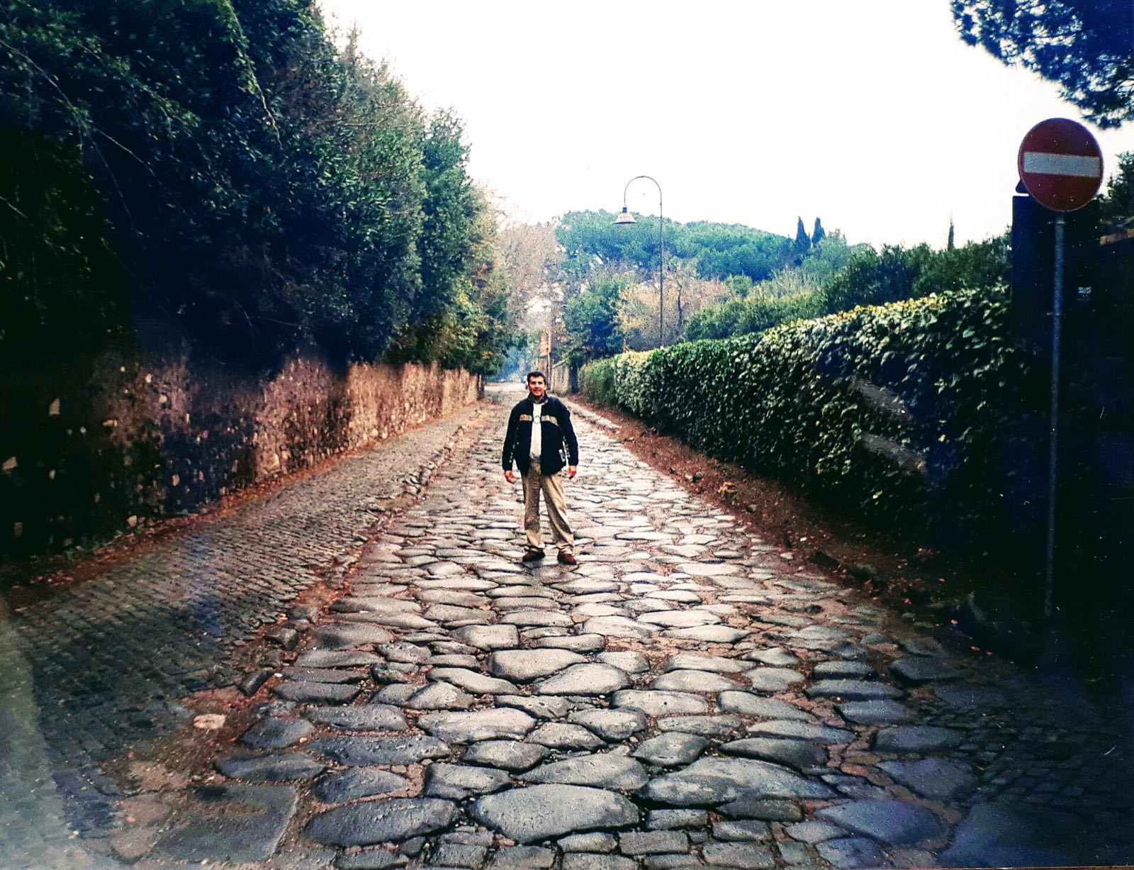 The ancient paving stones of the Appian Way, running between walls and trees.