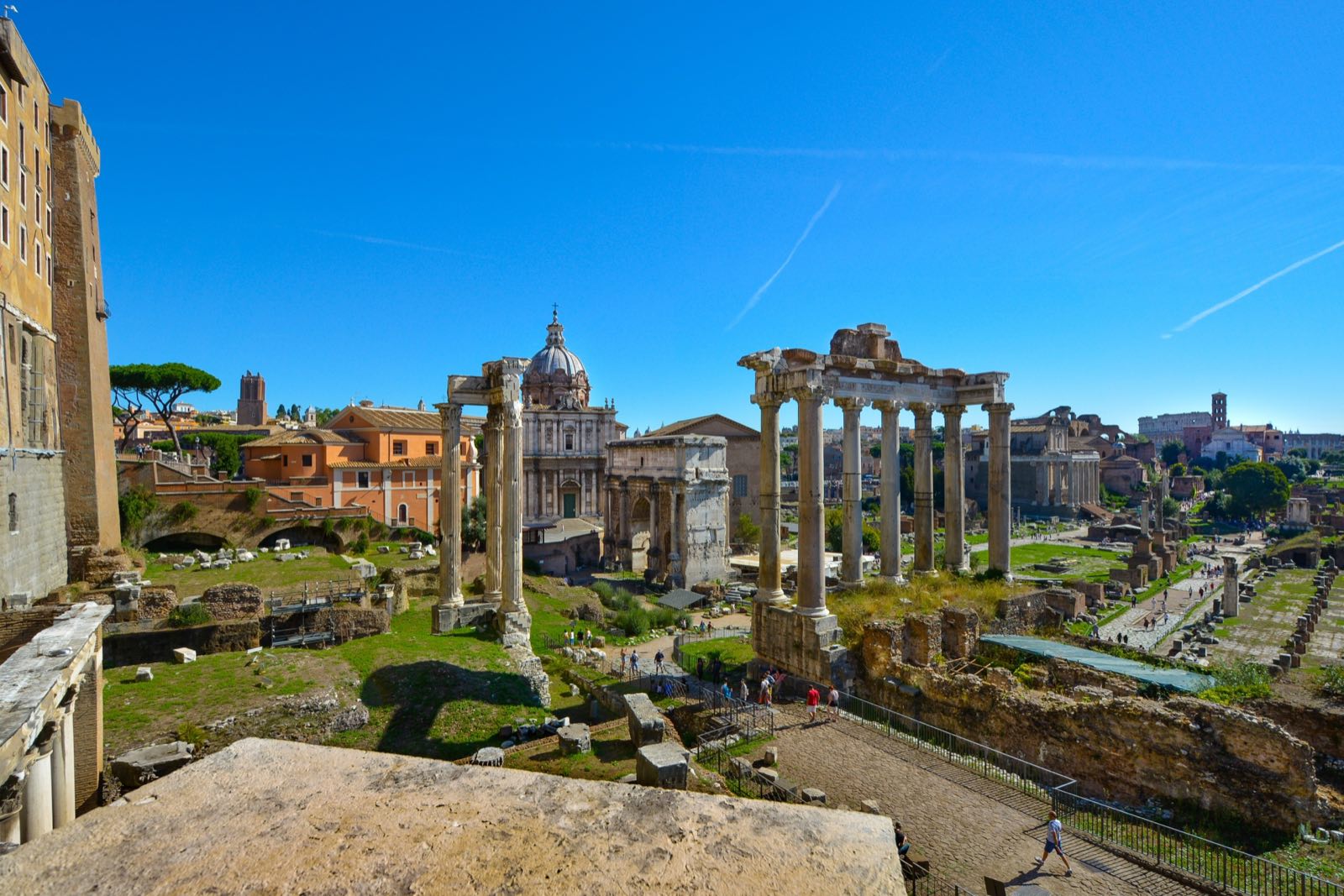 The columns and paving of the Roman Forum under a blue sky, seen from above.