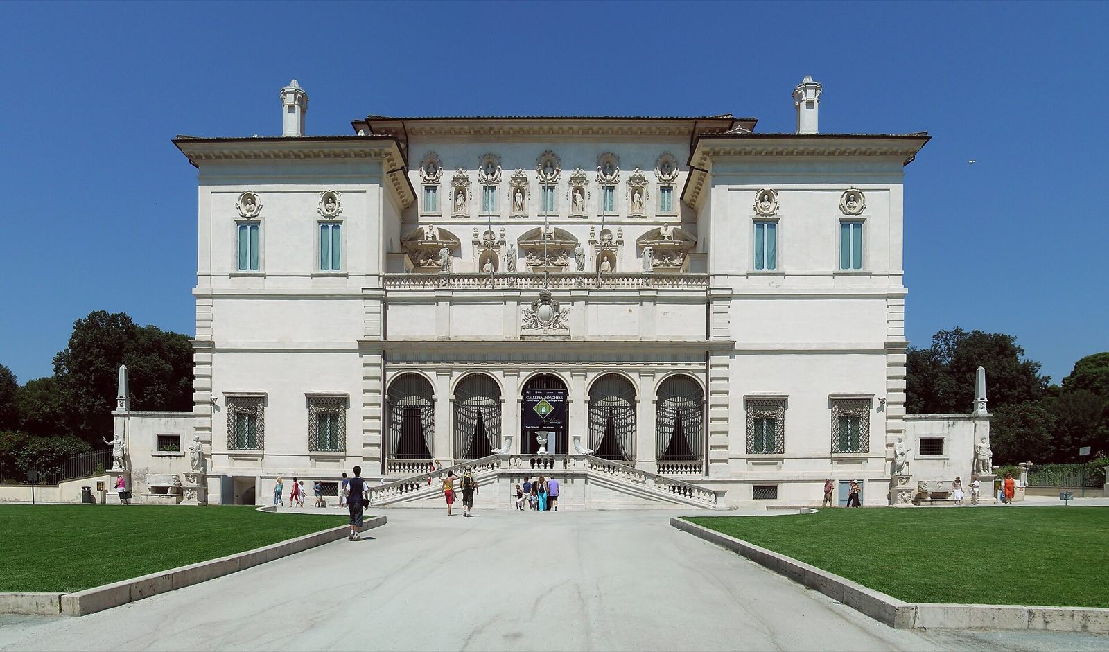 The white front of the Galleria Borghese, with its double staircase, at the end of a gravel court.