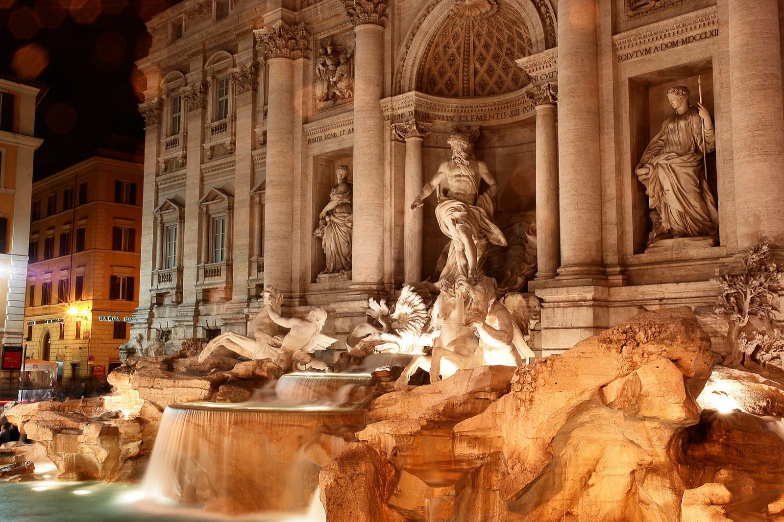 The Trevi Fountain lit at night, its statues golden above the water.